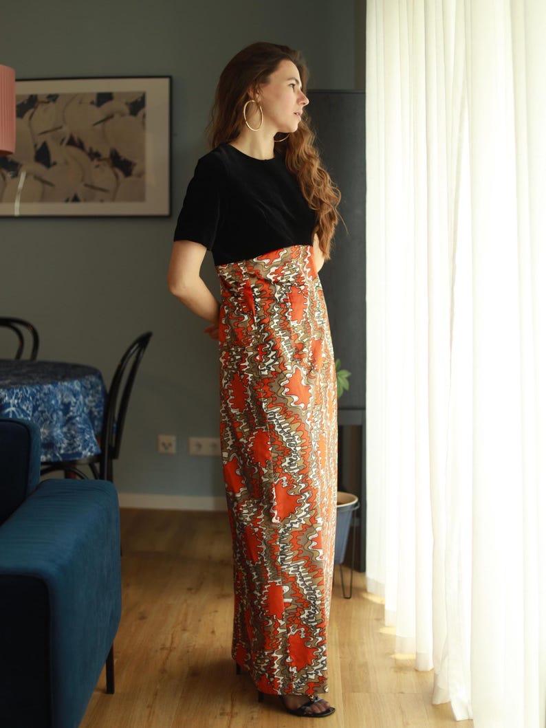 May include: A woman wearing a black velvet top with a long, orange and brown patterned skirt. The skirt has a swirling, abstract design.