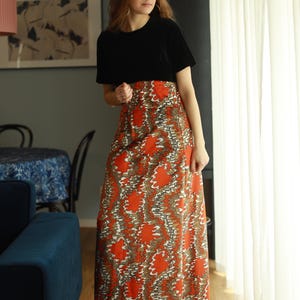May include: A woman wearing a black short-sleeved shirt and a long orange and brown patterned skirt. The skirt has a swirling, abstract design.