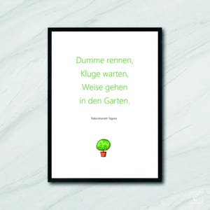 May include: A framed print with a white background and black frame. The print features green text that reads "Dummme rennen, Kluge warten, Weise gehen in den Garten." Below the text is the name "Rabindranath Tagore" and a small illustration of a green topiary in a terracotta pot.