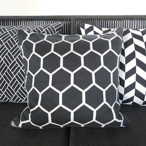 May include: Three decorative throw pillows with geometric patterns. The pillows feature black and white designs, including a honeycomb, chevron, and a diagonal grid. The pillows are square and appear to be made of a soft fabric.