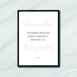 May include: A framed print with a black border, featuring the German text "Besondere Menschen erkennt man nicht, man fühlt sie." in a light gray script font. The print is on a white background.