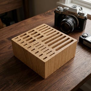 May include: A square light brown wooden organiser block featuring a series of rectangular slots of varying lengths and widths carved into the top surface, designed for holding multiple small items in an upright position.
