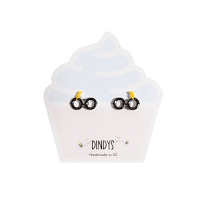 May include: Black and yellow stud earrings shaped like glasses with a lightning bolt detail. The earrings are displayed on a white cupcake-shaped card with the text "Dindys Handmade in US".
