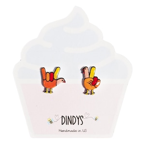 May include: A pair of colorful turkey earrings, one with a peace sign and the other with a rock and roll hand gesture. The earrings are on a white cupcake-shaped card with the text "Dindys Handmade in US".