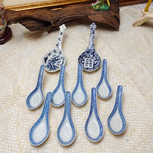 Könnte beinhalten: Eine Sammlung blau-weißer Keramik-Suppenlöffel. Zwei größere Löffel haben dekorative Griffe und detaillierte Muster. Die kleineren Löffel weisen ein Blumendesign innerhalb eines blauen Randes auf. Die Löffel sind auf einer strukturierten Oberfläche angeordnet.