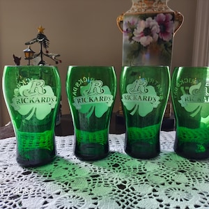 May include: Four green glass beer mugs with a white etched design of a shamrock and the text "Rickards" and the letter "R".