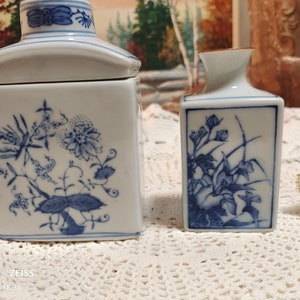 May include: Two blue and white porcelain vases with floral designs. The larger vase is a square jar with a lid. The smaller vase is a rectangular shape.
