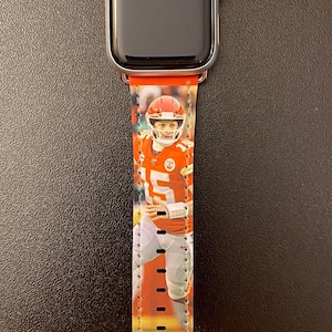 May include: A red and yellow Apple Watch band with a picture of a football player wearing a Kansas City Chiefs jersey. The band has the words "KC" and "CHIEFS" printed on it.