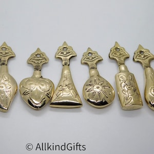 Peut inclure: Un ensemble de six cuillères en laiton poli aux formes de cuilleron variées, notamment en goutte, cœur, triangle, rond, rectangle et ovale. Chaque manche présente un sommet décoratif uniforme avec un trou et des motifs floraux gravés.