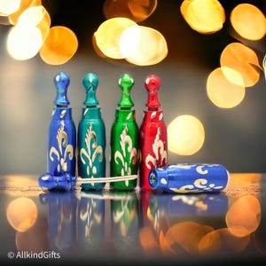 May include: Four small decorative bottles with gold accents and a floral design. The bottles are blue, green, and red. The bottles are on a reflective surface with a blurred background of yellow lights.