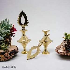 Pode incluir: Dois recipientes decorativos de metal dourado com topos ornamentados e uma peça decorativa de metal dourado separada com uma ponta pontiaguda.