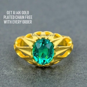 May include: A gold ring featuring a large, oval-shaped green gemstone. The ring has a delicate, intricate design.