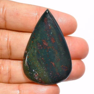 May include: A teardrop-shaped green, black, and red gemstone cabochon. The stone has a mottled pattern with red and black flecks throughout.