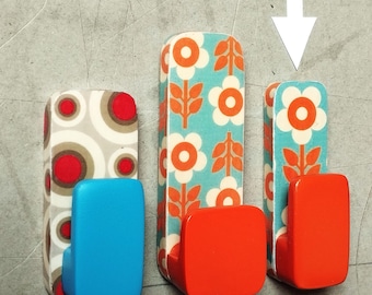 May include: Three decorative wall hooks with a retro floral design. One hook has a blue base, while the other two have red bases. The patterned sections feature white flowers and orange leaves on a teal background, and a gray, red, and white pattern.