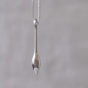 May include: A silver pendant necklace with a long, thin, teardrop-shaped pendant.