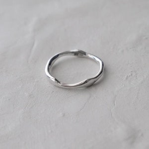 May include: A silver ring with a twisted, organic design. The ring is simple and elegant.