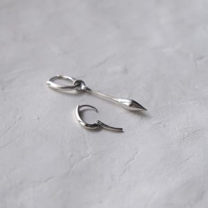 Può includere: Un paio di orecchini d'argento, uno è un cerchio e l'altro è un orecchino lungo, sottile e appuntito.