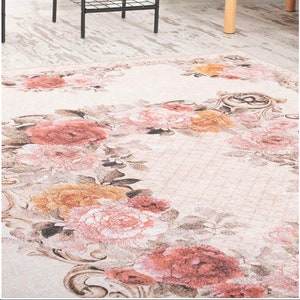 Könnte beinhalten: Ein floral gemusterter Teppich mit cremefarbenem Hintergrund und einem Rand aus rosa und orangefarbenen Rosen. Der Teppich hat einen Vintage-Look mit Gebrauchsspuren.