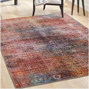 Könnte beinhalten: Ein mehrfarbiger Teppich mit einem abgenutzten, Vintage-Look. Der Teppich hat ein zentrales Medaillon-Design mit einem Rand aus komplizierten Mustern. Die Farben sind eine Mischung aus Rot, Orange, Blau und Grün.