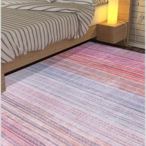 Könnte beinhalten: Ein gestreifter Teppich in den Farben Rosa, Orange und Grau. Der Teppich liegt vor einem Bett mit einem Holz-Kopfteil und gestreiften Bettwäsche.