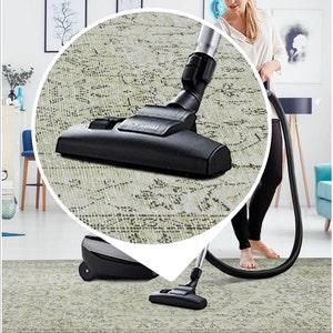 Pu&ograve; includere: Un aspirapolvere nero con un tubo di prolunga argentato viene utilizzato per pulire un tappeto beige chiaro con motivo. L'aspirapolvere ha un beccuccio nero e argentato con un accessorio a spazzola.