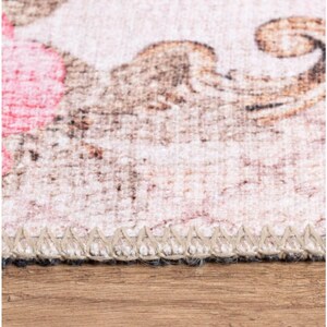 May include: Close-up of a beige rug with a floral pattern. The rug has a brown and white fringe border.