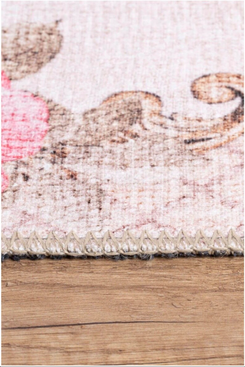 May include: Close-up of a beige rug with a floral pattern. The rug has a brown and white fringe border.