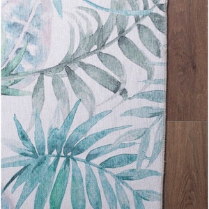 May include: A white rug with a watercolor design of blue and green palm leaves.