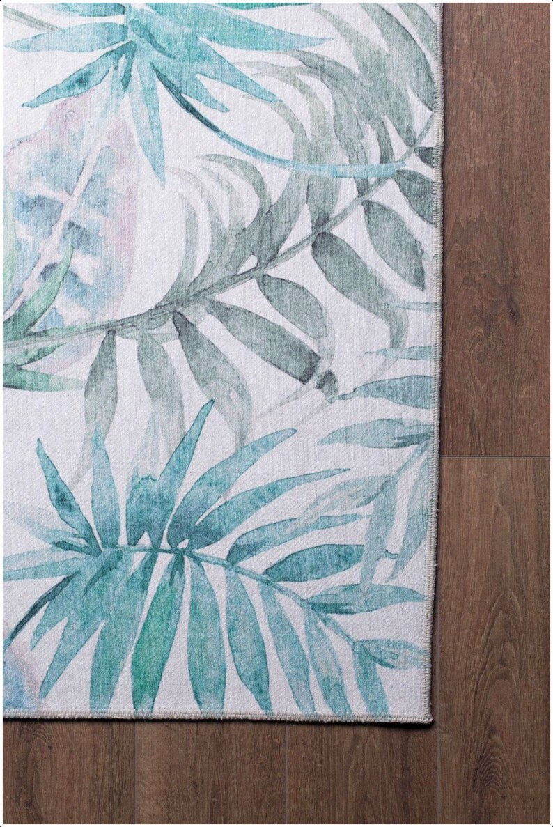 May include: A white rug with a watercolor design of blue and green palm leaves.