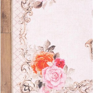 May include: A white rug with a floral design featuring pink, red, and orange roses. The rug has a brown, ornate border.
