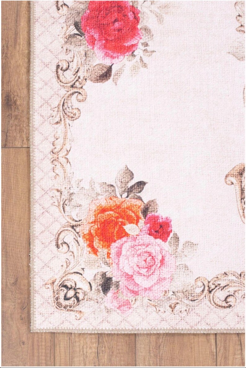 May include: A white rug with a floral design featuring pink, red, and orange roses. The rug has a brown, ornate border.