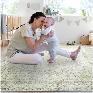 Pu&ograve; includere: Una donna e un bambino sono seduti su un tappeto a motivi verde chiaro e bianco. La donna indossa una camicia bianca e pantaloni bianchi. Il bambino indossa una camicia bianca e pantaloni grigi. Il tappeto ha un motivo floreale.