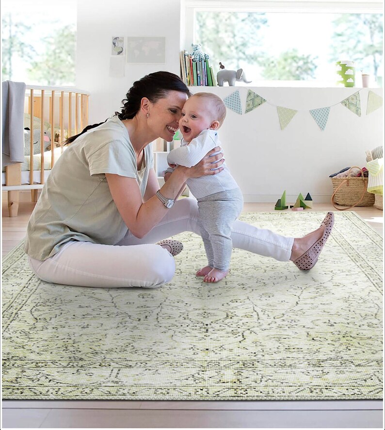 Pu&ograve; includere: Una donna e un bambino sono seduti su un tappeto a motivi verde chiaro e bianco. La donna indossa una camicia bianca e pantaloni bianchi. Il bambino indossa una camicia bianca e pantaloni grigi. Il tappeto ha un motivo floreale.