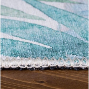 May include: Close-up of a teal and white patterned rug with a white fringe border. The rug is on a wooden surface.