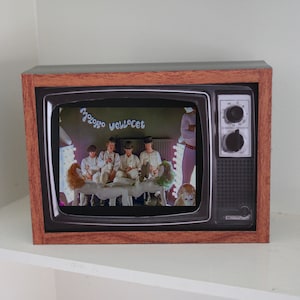 May include: A vintage-style television set with a brown wooden frame and a black screen. The screen shows a scene from the film "A Clockwork Orange" with the text "Mozgoro velvset" displayed on the screen.