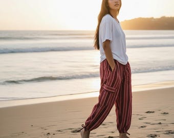 May include: A plain white short-sleeved t-shirt paired with loose-fitting, ankle-length trousers featuring a vertical striped pattern in shades of maroon, black, and white, complete with side cargo pockets and adjustable tie-cuff hems.