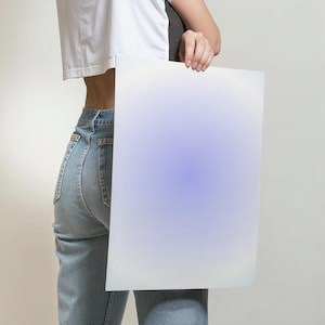 May include: A person holding a blank white poster with a light blue gradient in the center. The poster is held in front of the person's body, covering their torso and hips. The person is wearing blue jeans and a white shirt.