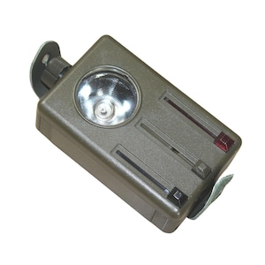 Op de afbeelding: Een groene zaklamp met een ronde lens en twee zwarte schakelaars. De zaklamp heeft een rood lampje aan de zijkant en een band om te dragen.