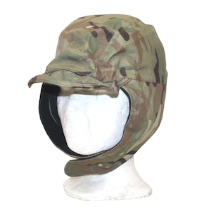 Op de afbeelding: Een camouflagepatroon hoed met een klep en oorflappen. De hoed is gemaakt van een stof met een mix van groene, bruine en bruinachtige kleuren. De oorflappen lopen door tot in de nek.