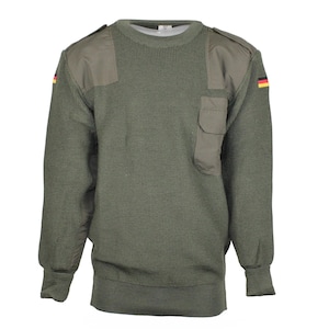 Może przedstawiać: Zielony sweter w stylu wojskowym z naszywką na każdym ramieniu i kieszenią po lewej stronie. Sweter ma okrągły dekolt i długie rękawy. Flaga Niemiec znajduje się na prawym rękawie.