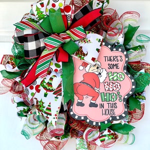 May include: A Christmas wreath with a red, green, and white color scheme. It features a sign that says "There's some Ho Ho Ho's in this house".