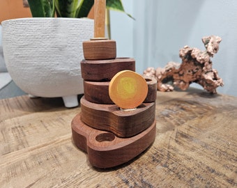 May include: A wooden stacking toy with a circular, orange and yellow piece on top. The toy is made of dark wood and has a natural finish.