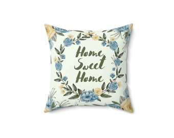 May include: Square throw pillow with a floral wreath design. The wreath features blue and yellow roses, surrounding the words "Home Sweet Home" in a script font. The pillow has a light green background.