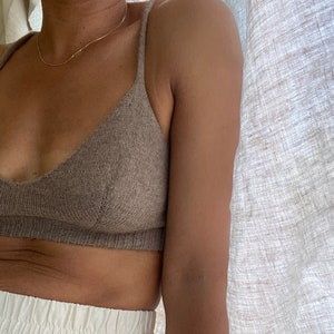 Puede incluir: Un bralette de punto marrón con tirantes finos. El bralette lo lleva una persona con un collar de cadena dorada.