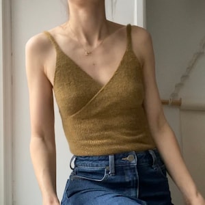 Puede incluir: Un top de tanque de punto amarillo mostaza con escote en V y tirantes finos. El top se lleva con jeans azules.