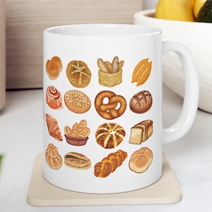 May include: White ceramic mug with a colorful illustration of various breads and pastries. The mug has a handle on the right side.