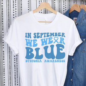 Puede incluir: Camiseta blanca con texto azul que dice "En septiembre usamos azul" y "Concientización sobre la distonía".