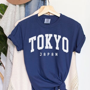 Pode incluir: Uma camiseta azul marinho com texto branco que diz "TOKYO JAPAN".