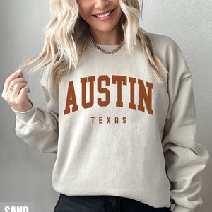May include: A sand-colored sweatshirt with the text "AUSTIN TEXAS" printed in brown on the front.