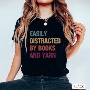 May include: Black t-shirt with the text "EASILY DISTRACTED BY BOOKS AND YARN" in a rainbow color scheme.